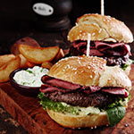 Gourmet Tasty Steak Burgers with Ham Slices on a Wooden Tray with Potato Wedges and Dipping Sauce.