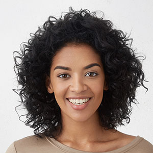 Cheerful dark-skinned girl smiling broadly, rejoicing at her victory in competition among young writers, standing isolated against grey wall background. People, success, youth and happiness concept