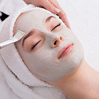 Face peeling mask, spa beauty treatment, skincare. Woman getting facial care by beautician at spa salon, side view, close-up